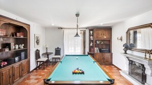 Een biljartkamer met een pooltafel, houten kasten en een open haard.