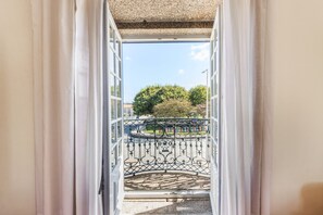An open doorway leading to a balcony with a wrought iron railing, a clear sky, and trees in the background.