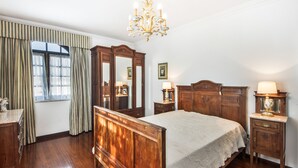 Een klassieke slaapkamer met een houten bed, een kroonluchter, een dressoir en een spiegel.