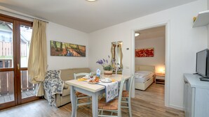 A dining area with a table set for two, a sofa, and a bed in the background. - Apartment 'Rosa delle Dolomiti Bilocale2' with Mountain View and Wi-Fi (Carisolo)