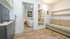 A compact living space with a kitchenette, a bed, a sofa, and a mirror. - Apartment 'Rosa delle Dolomiti Bilocale2' with Mountain View and Wi-Fi (Carisolo)