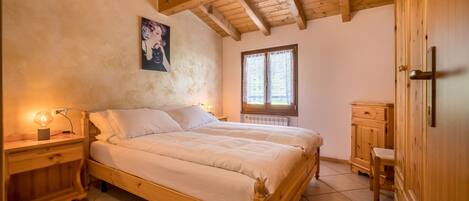 A wooden bed in a room with a sloped ceiling and a window.