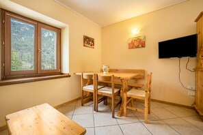 A dining area with a wooden table and chairs, a window with a view of trees, and a television mounted on the wall.