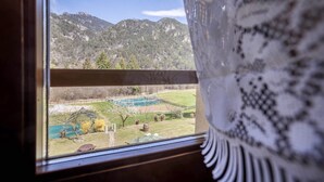 A window view of a mountainous landscape with a swimming pool and a wooden deck.