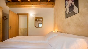 A bedroom with a wooden ceiling, a bed with white bedding, a wooden door, and a wall-mounted mirror.