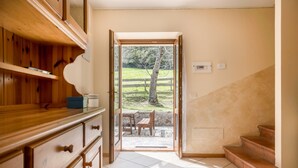 A room with a wooden cabinet, a tiled floor, a staircase, and a door leading to an outdoor area with a table and chairs.