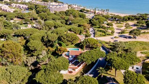 Luchtbeeld van een kustgebied met woningen, een zwembad, weelderige begroeiing en een strand op de achtergrond.
