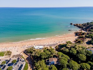 An aerial view of a beach with a parking area, a building, and dense greenery.