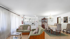 A living room with a sofa, coffee table, dining table, chairs, and a kitchen area in the background. - Holiday Home 'Moinho De Paradela' with Private Pool, Private Terrace and Wi-Fi (Paradela)
