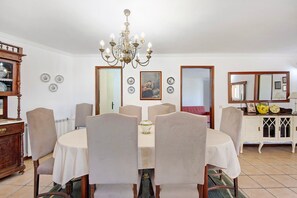 Comedor con una mesa redonda, sillas, una lámpara de araña y un aparador con objetos decorativos.