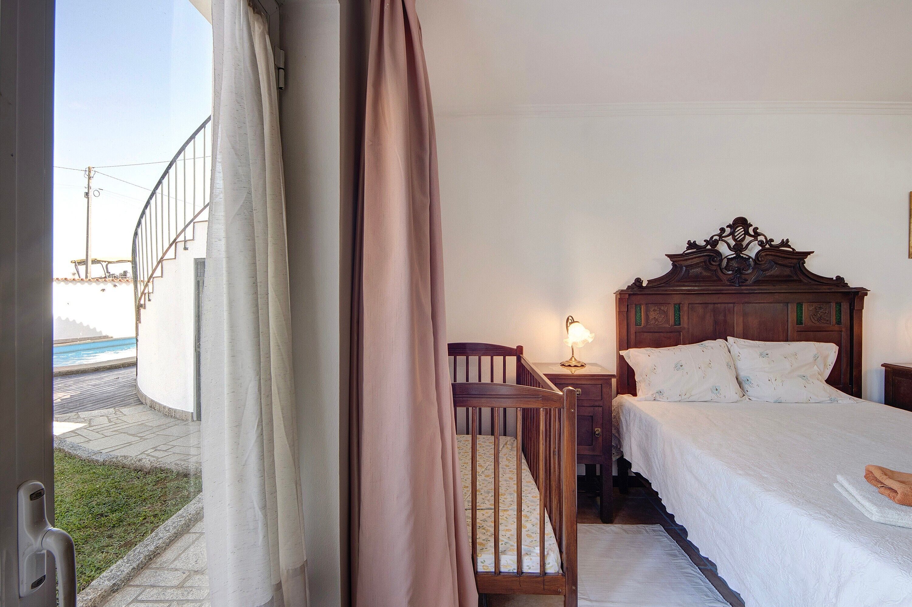 Quarto com cabeceira de madeira, mesa de cabeceira com abajur e vista para o exterior.