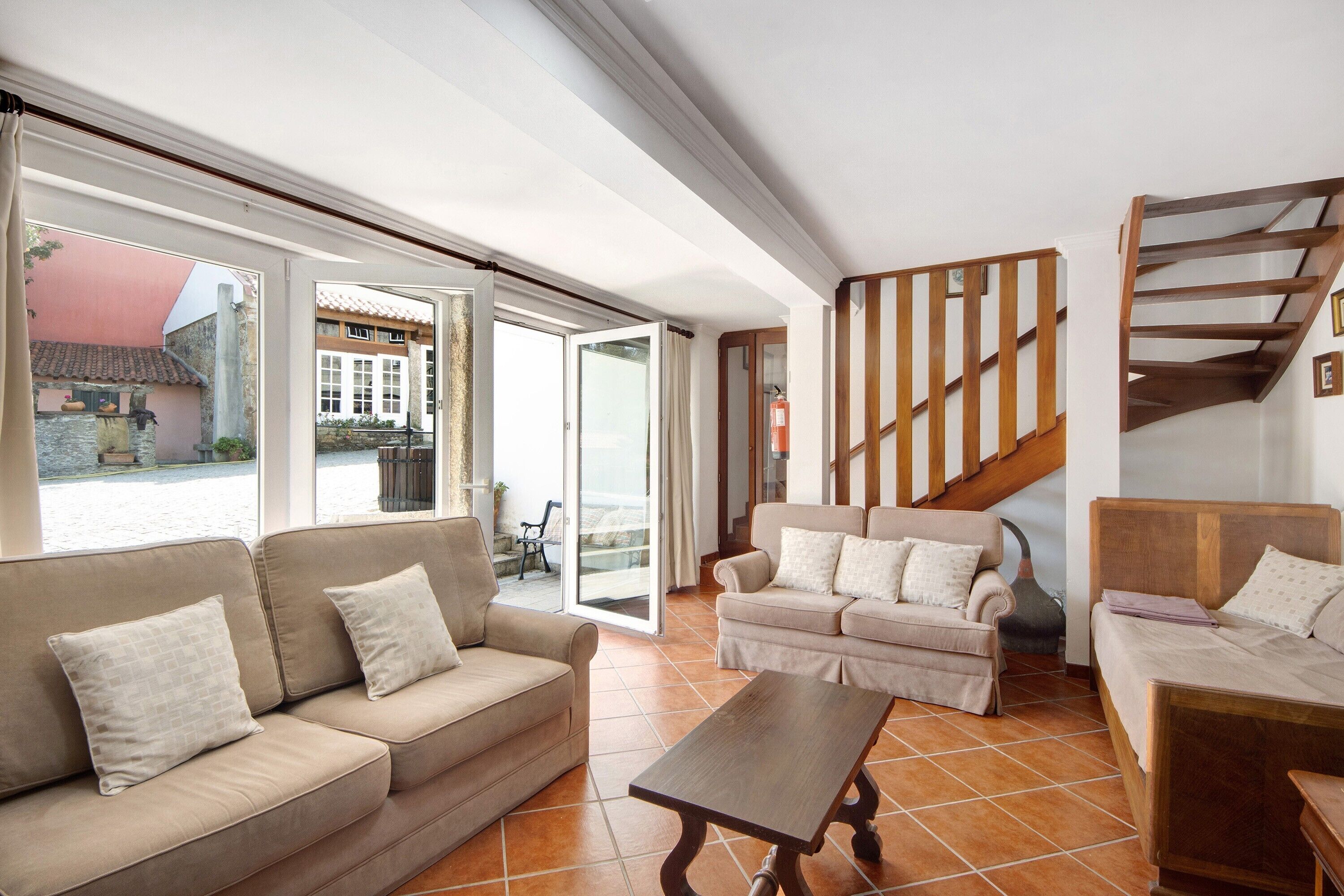 Ein großzügiger Wohnbereich mit Sofa, Sessel und Couchtisch, einer Holztreppe und großen Schiebeglastüren, die auf eine Außenpatio führen.