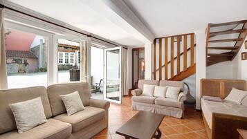 Ein großzügiger Wohnbereich mit Sofa, Sessel und Couchtisch, einer Holztreppe und großen Schiebeglastüren, die auf eine Außenpatio führen.