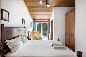Un dormitorio con techo de madera, una cama con cabecera, una silla, una mesita de noche y un armario.