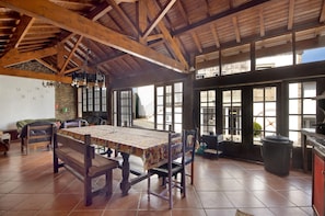 Un comedor rústico con mesa y sillas de madera, ventanas amplias y una pared de piedra.