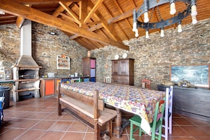 Una cocina rústica con pared de piedra, vigas de madera, horno empotrado y una mesa de comedor con mantel de colores.