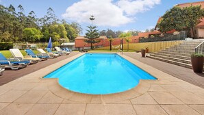Une piscine rectangulaire, bordée d’une terrasse carrelée, entourée de chaises longues et de plantes en pot.