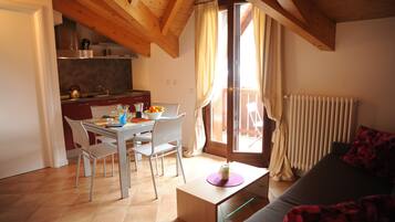 Un coin repas avec une table et des chaises, une cuisine à l’arrière-plan et un espace de vie avec un canapé et une fenêtre.