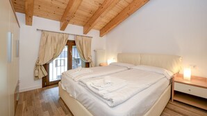 Ein Schlafzimmer mit Holzboden, einem großen Bett mit weißen Leinentüchern, einem Nachttisch mit Lampe und einem Fenster mit Vorhängen.