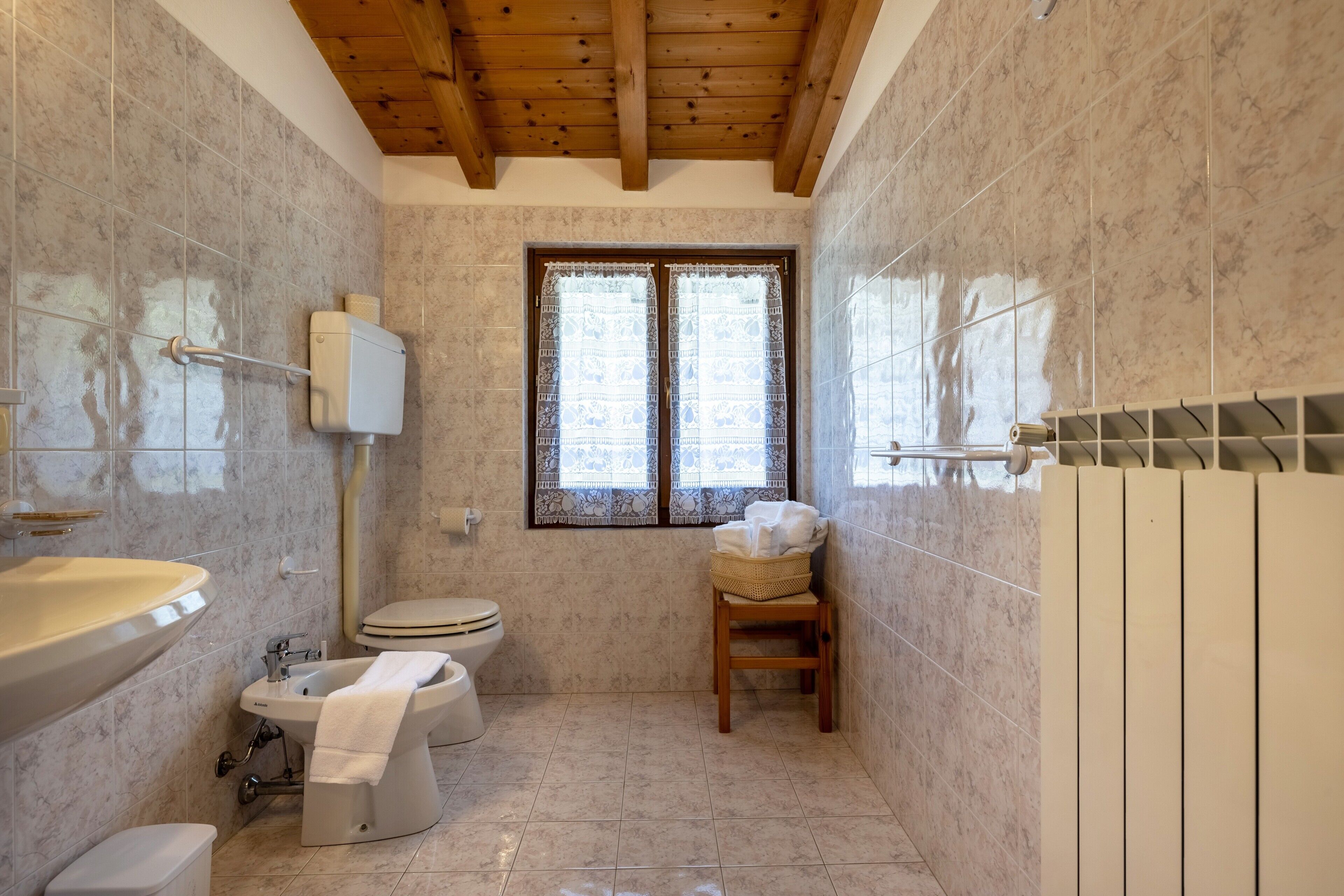 Ein Badezimmer mit Toilette, Bidet, Waschbecken und einem Fenster mit gemusterten Vorhängen.