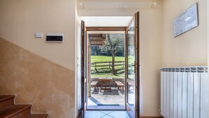 Un couloir avec un escalier, une porte donnant sur un patio extérieur avec une table et des chaises, et un radiateur fixé au mur.