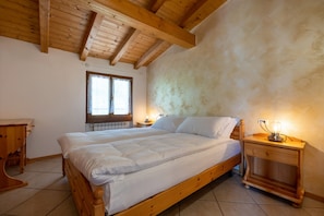 A bedroom with a wooden bed, a nightstand with a lamp, a window, and a radiator.