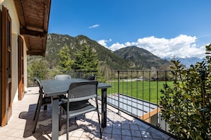 A balcony with a table and chairs, a view of a green field, and mountains in the background.