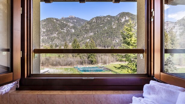 Une pièce dotée d’une grande fenêtre, de poutres en bois et offrant une vue sur les montagnes et une piscine.