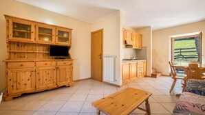 Eine Küche mit Holzausstattung, ein Essbereich mit Tisch und Stühlen sowie ein Blick auf eine grüne Landschaft durch ein Fenster.
