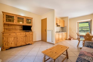 Une cuisine avec des meubles en bois, un coin repas avec une table et des chaises, et une vue sur un paysage verdoyant par la fenêtre.