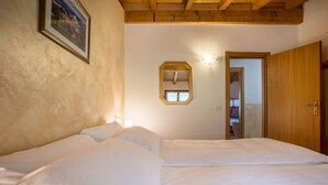 Ein Schlafzimmer mit Holzbalkendecke, einem Bett mit weißer Bettwäsche, einem gerahmten Bild an der Wand und einem Spiegel.