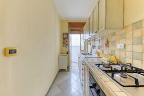 Une cuisine équipée d’une cuisinière à gaz, de placards, d’un petit réfrigérateur et d’un plan de travail recouvert de carreaux.