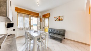 A dining area with a table and chairs, a sofa, and a television mounted on the wall. - Holiday Apartment "Baia Del Mare" with 2 Private Terraces, Private Garden & A/C (Lido Marini)