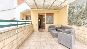 A covered outdoor area with a stone wall, a green railing, and wicker furniture. - Holiday Apartment "Baia Del Mare" with 2 Private Terraces, Private Garden & A/C (Lido Marini)