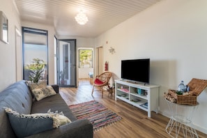 Una sala de estar con sofá, televisor, cesta de mimbre y estantería blanca.