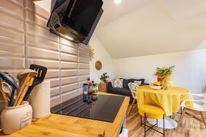Une cuisine moderne avec un plan de travail noir, des carreaux blancs et un coin repas agrémenté d’une nappe jaune.