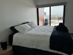 Relax in a spacious bedroom with a large bed, a bedside table, and a sliding door leading to a balcony with city views.