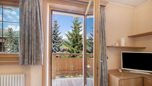 Una habitación con puerta corrediza de vidrio a un balcón, un armario de madera y un televisor sobre un mueble.