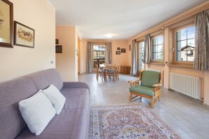 A living room with a sofa, a chair, a dining table, and a patterned rug.