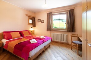 A bedroom with a wooden bed, a window with curtains, a radiator, and a chair.