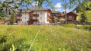 Un hotel con varios balcones, un campo de flores silvestres y montañas al fondo.