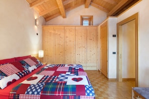 A bedroom with a wooden ceiling, a large bed with a quilt, a wardrobe, and a door.