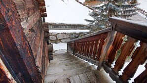 Uma escadaria de madeira leva a uma parede de pedra, com o chão coberto de neve e uma árvore.