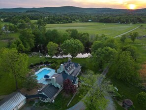 A large house with a swimming pool, surrounded by lush greenery and a lake. - Buckskin Manor - Historic, Pool, 66 Acre Vineyard (Purcellville)