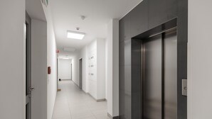 Un pasillo moderno con suelo de baldosas, una puerta a la izquierda y un ascensor a la derecha.