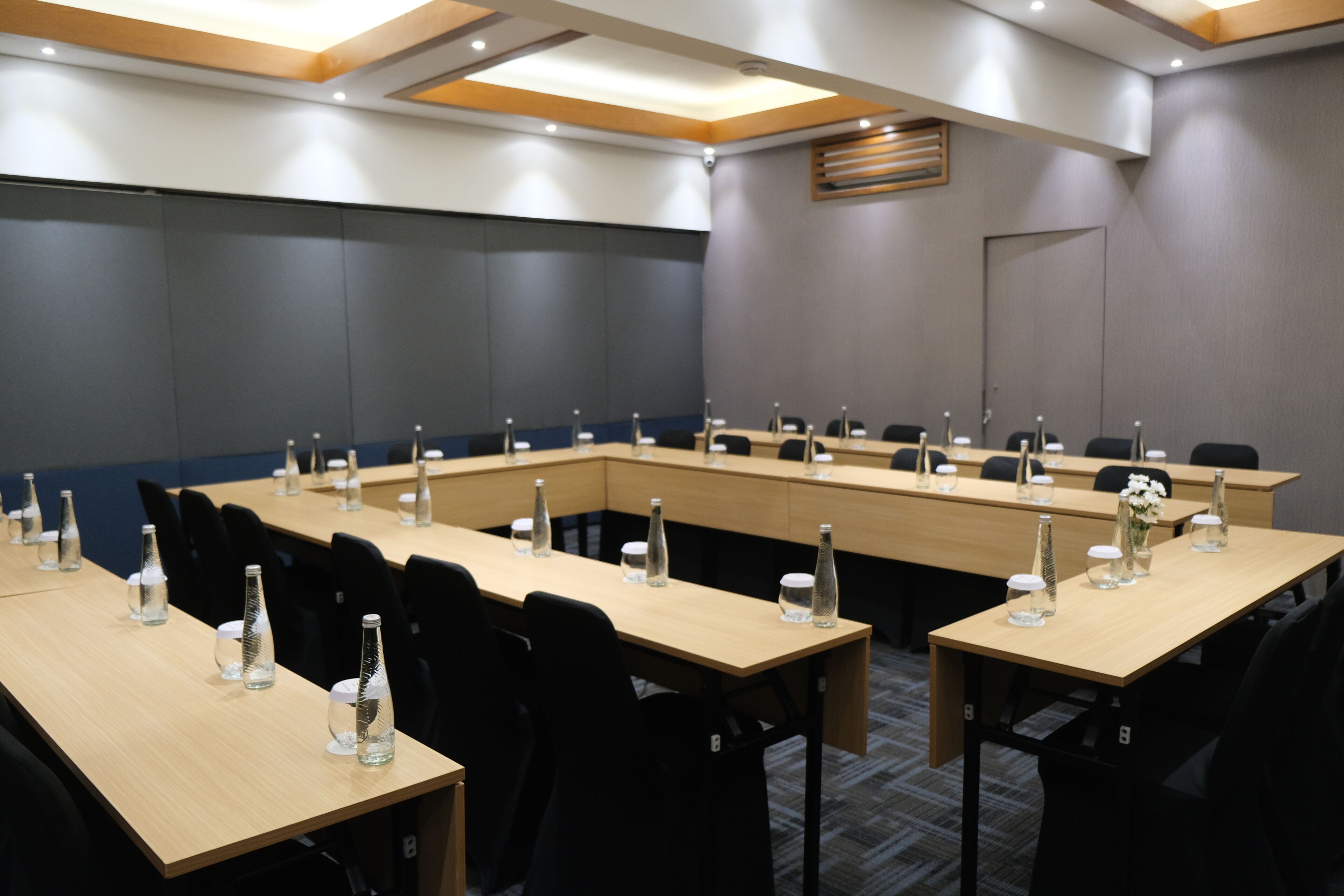 Un salón de conferencias con largas mesas, sillas y botellas de agua.