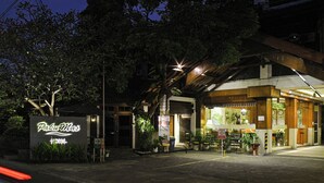 Hotel llamado "Paku Mas" con letrero, zona de estar al aire libre y entrada cubierta.