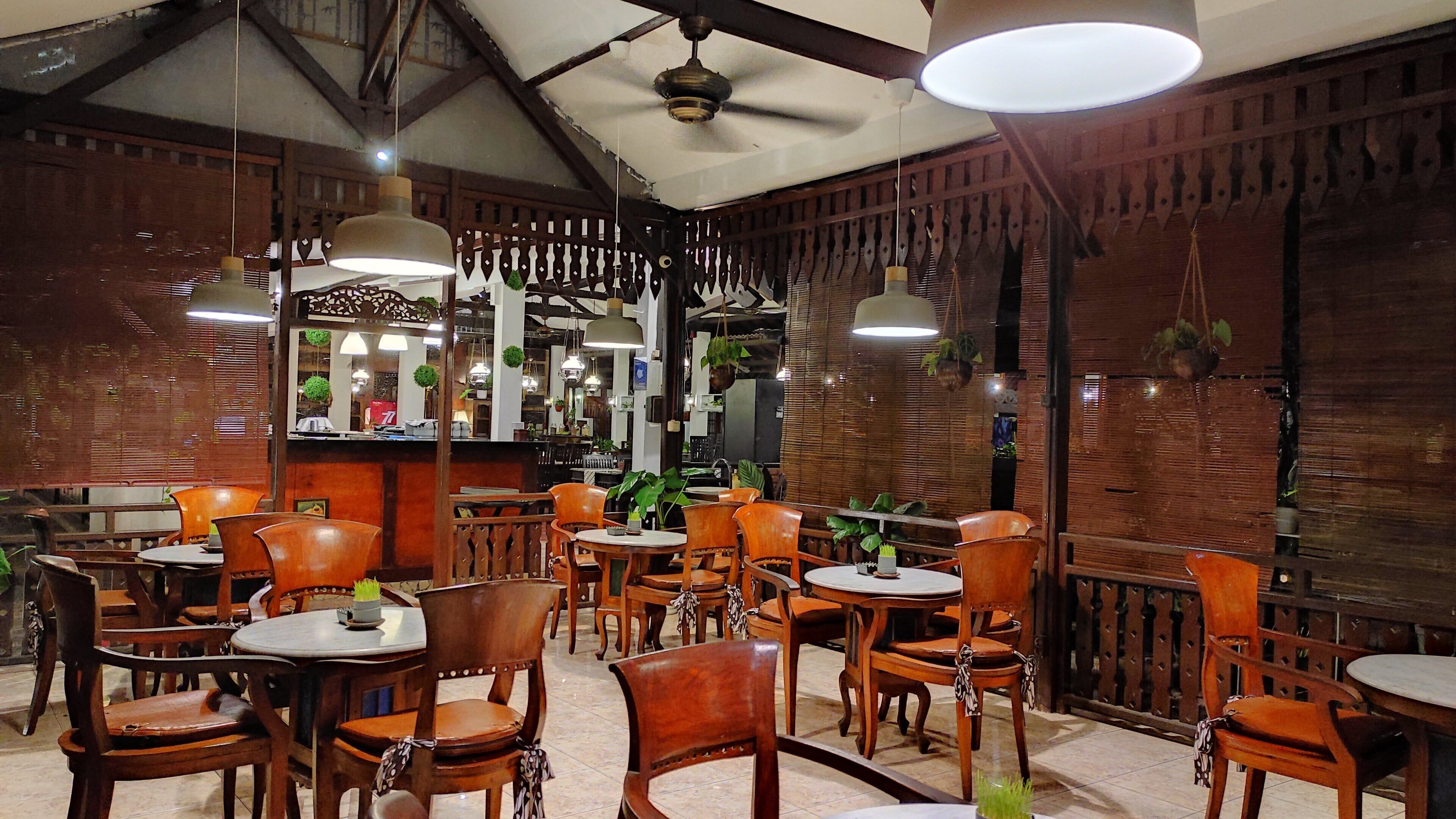 Interior de restaurante con mobiliario de madera, plantas colgantes e iluminación colgante.