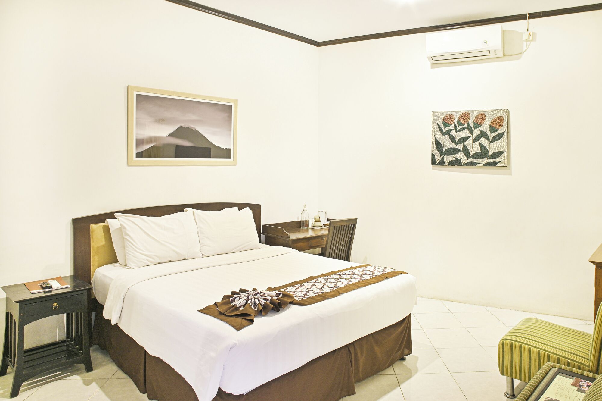 A hotel room with a bed, bedside tables, a nightstand, a chair, and artwork on the walls.