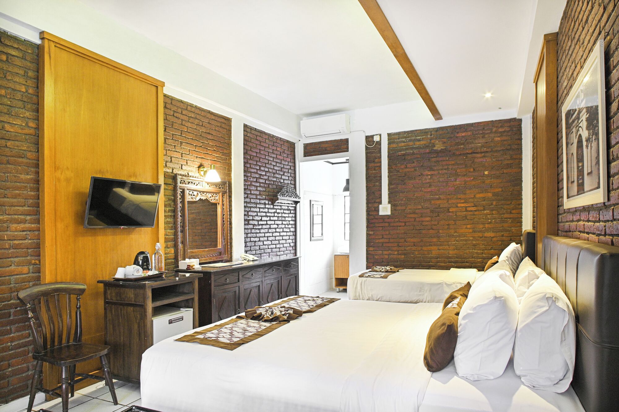 A hotel room with a large bed, a desk with a chair, a TV, and a brick wall.